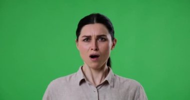 Kafkasyalı üzgün bir kadın yeşil arka planda duruyor, üzgün ve isteksiz görünüyor. Bir şeyi reddediyor, hayır diyor ve açıkça gördüklerinden memnun değil..