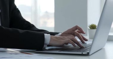 Yakından bakıldığında, siyah iş ceketi giymiş, dizüstü bilgisayarda ustalıkla yazı yazan kararlı bir Hintli iş kadınının elleri görülüyor. Masa dağınık belgelerle süslenmiş..