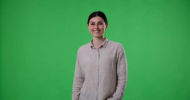Beyaz ırktan neşeli bir kadın yeşil perde arkasında duruyor ve onayını ve memnuniyetini baş parmak işareti yaparak gösteriyor.
