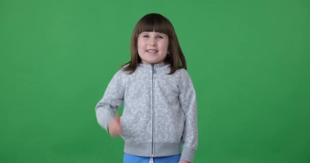 かわいい就学前の女の子は カメラを見て笑って 緑色の画面に立っています 彼女は腕を上げて親指を立てて何かの承認や好みを示す — ストック動画