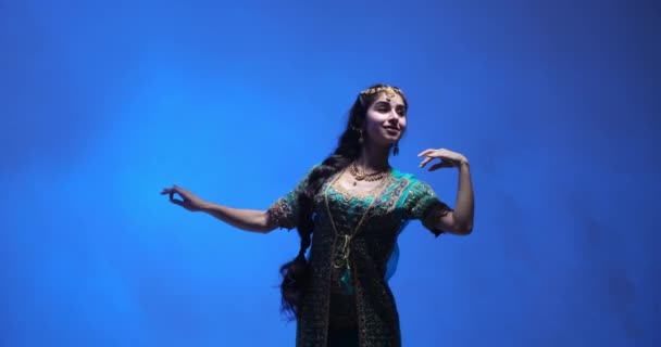 インドの女性は青いスタジオを背景に伝統的なインド舞踊を披露した 美しい緑と金のサリーに身を包んだ彼女は 伝統的なインドのジュエリーで飾られています 彼女の顔に笑顔で — ストック動画