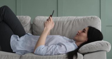 Kanepede uzanmış, yüzünde kocaman bir gülümsemeyle cep telefonuyla mesajlaşan neşeli beyaz bir kadın. Boş zamanlarının tadını çıkartıyor, iyi bir ruh hali içinde, pozitif titreşimler yayıyor..