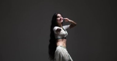 Bu yetenekli Hintli dansçı güzel beyaz bir sari içinde karmaşık detaylar ve ışıltılı mücevherlerle. Karanlık bir arka planda performans sergiliyor ve güzelliği ve zarafetiyle büyüleniyor..