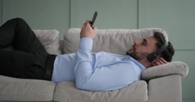 Kafkasyalı bir adam, kulaklığı ve elinde telefonuyla kanepede uzanır. Telefonunu karıştırıyor ya da tamamen müziğine dalmışken daktilo yazıyor.
