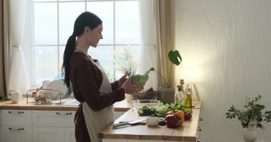 Mutfak önlüklü neşeli beyaz kadın mutfağa pozitif enerji getiriyor. Bulaşıcı gülümseme, neşeli yemek pişirme havasını belirler. Özenle ahşap kesme tahtasıyla lahana doğruyor..