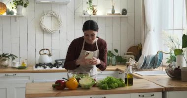 Beyaz kadın mutfağında durmuş taze salatasının görsel ziyafetini yakalıyor. Sosyal medya takipçilerinin tadını çıkarması için mükemmel bir görüntü yakalıyor..