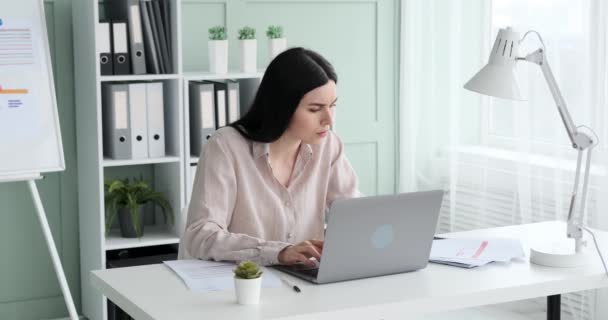 身穿衬衫的白人女商人坐在办公桌前 在笔记本电脑上打字 她因工作而感到疲倦和困倦 把手放在太阳穴上 感到头疼 — 图库视频影像
