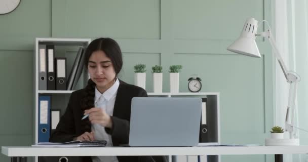 一位开朗的印度女商人 穿着黑色商务夹克和白衬衫 在笔记本电脑上工作 她的长发在认真审阅文件 做笔记和更新资料的过程中逐渐褪了色 — 图库视频影像