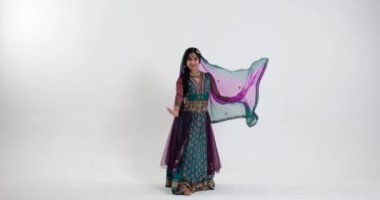 Yetenekli bir Bharatanatyam dansçısı zarif hareketler ve karışık jestlerle geleneksel Hint mücevherleri ile canlı bir sari giyerek yeteneklerini sergiliyor. Beyaz arkaplanda dans.