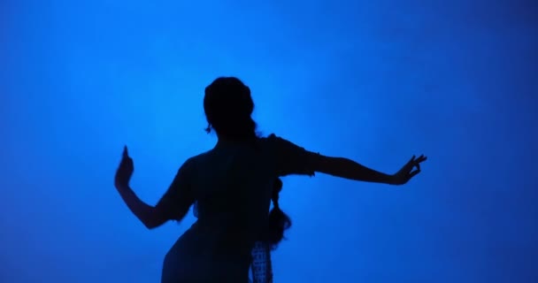 在醒目的蓝色背景下 一位身着莎丽服的年轻女子表演的动作凸显了这种古老艺术形式的流畅与优雅 剪影增添了一丝神秘感和诱惑 — 图库视频影像