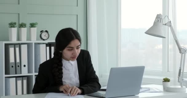 一位穿着正装的印度职业女性坐在她的办公桌前 她脸上挂着温暖的笑容 全身心地投入到工作中 勤奋地阅读笔记本电脑上的文件 — 图库视频影像