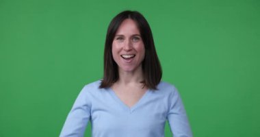 Neşeli kadın yeşil ekran arka planında duruyor, elleri gözlerinin yanında dürbünlü bir jest yapıyor. Bir şey arıyor gibi görünüyor ve şaşırdığını ve şaşırdığını ifade ediyor.