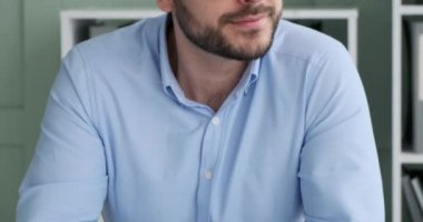 Resmi giyinmiş ve gözlüklü beyaz iş adamı ofisinde masasında otururken görülüyor. Pencereden dışarı bakıyor, sonra kameraya bakıyor ve dişleriyle geniş bir gülümseme sergiliyor..