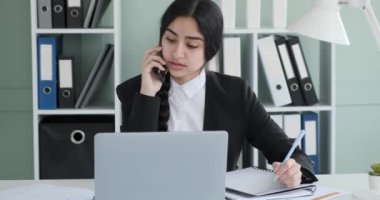 Ofis masasında oturan Hintli iş kadını, tamamen işe dalmış. Çok zahmetsizce, önemli iş meselelerini çözmek için telefonda konuşurken özenle not defterine not alıyor..
