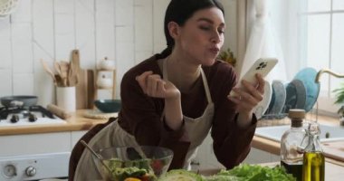Kafkasyalı bir kadın, rahat bir mutfakta, bir kaseden nefis bir salatanın tadını çıkarırken telefonla meşgul oluyor. Onun gevşek davranışı modern bir yaşam tarzını resmediyor..