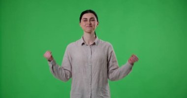 Beyaz bir kadın yeşil perde arkasında durup evet diye bağırıyor ve ellerini havaya kaldırarak zaferi kutluyor. O heyecanı ifade ederken dirsekleri bükülmüş ve yumrukları sıkılmış..