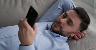 Kanepede uzanmış, işe dalmış ya da telefonunu karıştıran beyaz bir adam. Çok sakin ve rahat görünüyor. Huzur ve rahatlığın tadını çıkarıyor..