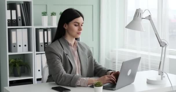 一位穿着衬衫和夹克 自信专注的女商人坐在办公桌前 在笔记本电脑上打字 脸上挂着淡淡的微笑 她看上去很舒服 很有控制力 工作做得很有效率 — 图库视频影像