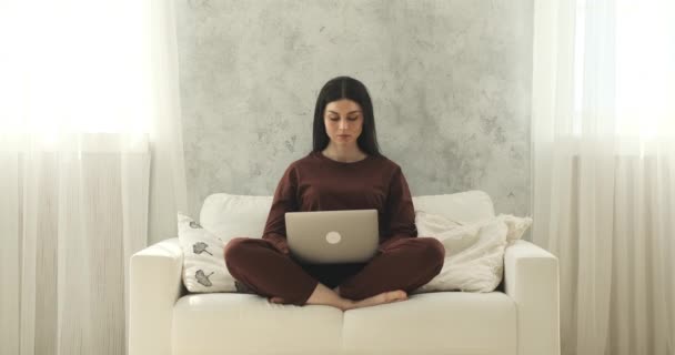 ソファに座っているパジャマ姿の白人女性がノートパソコンで仕事に没頭していた 真剣で自信に満ちた表情で 彼女は簡単にタスクやプロジェクトをナビゲートします — ストック動画