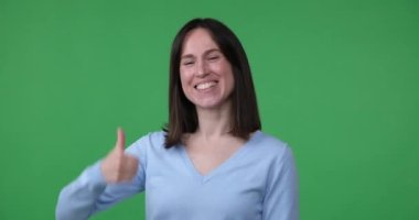 Yeşil ekran arka planında duran neşeli beyaz bir kadın yüzünde geniş bir gülümsemeyle kocaman bir jest gösteriyor. Onaylıyor ve bir şeyden hoşlanıyor..