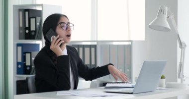 Ofisindeki bir masada oturan Hintli kadın özenle çalışıyor ve bir telefon görüşmesi yapıyor. Birden fazla iş yaparken, telefonda konuşurken profesyonellik ve yeterlilik sergiliyor..