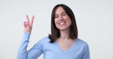 Beyaz arka planda beyaz bir kadın duruyor, eliyle zafer işareti gösterirken parlak bir gülümseme sergiliyor. Ziyaretçi işareti bir zafer ya da barış işareti..