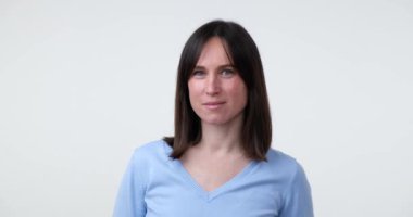 Çekici bir gülüşü olan güzel beyaz bir kadın beyaz bir arka planda kameraya bakıyor. Kollarını göğsünde kavuşturur, kendine güven ve pozitiflik gösterir..