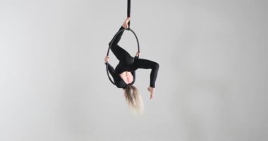 Hava halkasındaki yetenekli beyaz bir kadından büyüleyici bir dans gösterisi. Gri bir arkaplanda, sanatını ve gücünü siyah bir tulum ve yalınayak sergiliyor..