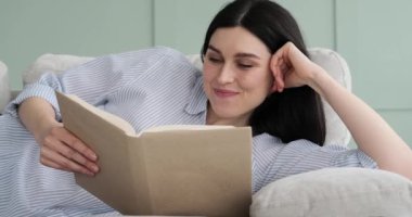 Etnik kökenli gülümseyen beyaz bir kadının portresi bir kanepede uzanıyor ve iyi bir kitap okumanın keyfini çıkarıyor. Kitabının sayfalarında kaybolurken rahat ve hoşnut bir hava yayıyor..