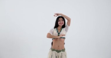 Genç bir Hintli kadın, beyaz sari ve geleneksel takılarla dans ederken neşe ve enerji saçıyor. Performansı hayatın, hareketin ve Hint kültürünün gerçek bir kutlaması..