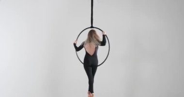 Akrobatik hünerini hava çemberinde sergilerken kendine güvenen beyaz bir dansçı. Çarpıcı bir siyah tulum ve yalınayak havada zahmetsizce hareket ediyor..