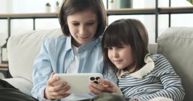 Kardeş kanepede birlikte oturur. Yüzlerini aydınlatan neşeli gülümsemelerle, telefon kullanıyorlar, şaşırtıcı bir şey görüyorlar, gözleri şaşkınlıkla genişliyor, ve Wow diye bağırıyorlar dudaklarından kaçıyorlar..