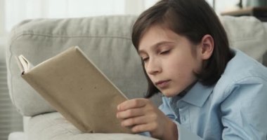Kitapların büyüleyici dünyasında avuntuyu bulan bir çocuk. Genç çocuk kanepede rahat bir şekilde yatarken görülüyor, yüzünü süsleyen bir gülümseme, büyüleyici bir kitabın sayfalarına sarılmış..