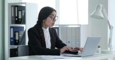 Ofis masasında oturan Hintli kadın, özenle dizüstü bilgisayarı üzerinde çalışıyor, güzel bir haber alıyor, gülümsüyor, vay canına diyor ve olumlu gelişmeyi kutluyor..