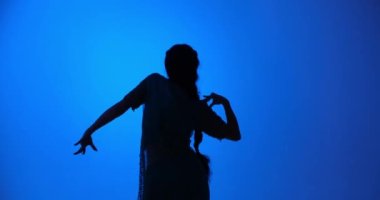 Geleneksel Hint dansını gösteren genç bir Hintli dansçının silueti. Sarisi ve hünerli hareketleriyle, mavi arka planda seyirciyi keyiflendirir..