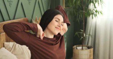 Pijamalı beyaz bir kadının huzur içinde yatağında oturup keyifli bir şekilde uyandığı hoş bir sahne gözler önüne seriliyor. Mutlu bir gülümseme ile, gerinir ve ferahlatıcı bir sabah esnemesinin tadını çıkarır..