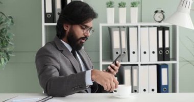 Yavaş çekimde, Hintli bir işadamı ofisinde oturup, interneti kolaçan ederken bardaktan sıcak bir içecek yudumluyor. Bardaktan yükselen sıcak buhar rahat ve rahatlatıcı bir atmosfer yaratır..