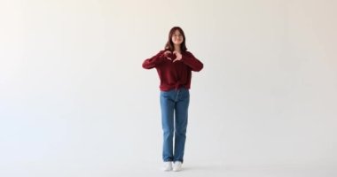 Genç kız, ellerini beyaz bir arkaplana dayayarak kalp şeklinde yaparak sevgi ve pozitiflik yayar. Sıcak bir gülümseme ve samimi bir jestle aşkın ve sevginin simgesini oluşturuyor..