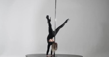 Büyüleyici beyaz bir kadın tarafından yapılan baştan çıkarıcı direk dansı. Gri bir arkaplanda, siyah tulumu ve yüksek topuklularıyla özgüven ve şehvet yayıyor..