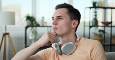 Adam evindeki rahat koltukta rahat bir şekilde oturuyor. Derin düşüncelere dalmış, kaşları hafifçe çatılmış ve bakışları uzak bir noktaya odaklanmış..