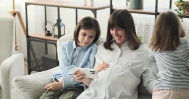 Hamile bir anne ve iki çocuğu sıcak oturma odasında bir araya geliyorlar. Kanepede oturan anne, oğlu ve kızıyla birlikte telefon ekranına takılmış..