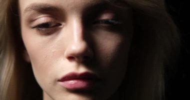 Siyah arka planda üzgün, beyaz bir kadın, yüzü yoğun ve detaylı bir portrede ortaya çıkıyor. Düşünceli bir ifade ve kederle dolu gözlerle duyguları aşikar..