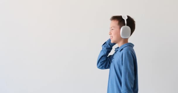 アジア系の少年は 純白の背景に魅惑的なメロディーで失われました 彼の耳を受け入れる洗練されたヘッドフォンのペアで 彼は音楽と一つになります — ストック動画