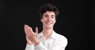 Gösterişli, siyah bir arkaplanda, mutlu beyaz bir adam coşkuyla alkışlarken yakalanıyor, yüzü zevkten kıpır kıpır parlıyor. Alkışları açık bir onay ve takdir göstergesidir..