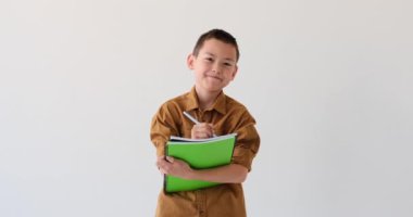Asyalı çocuk beyaz arka planda yazma eylemine girişiyor. Elinde bir defterle, çocuk hevesle düşüncelerini, fikirlerini ve gözlemlerini kağıda yansıtıyor..