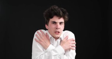 Siyah bir arka planda, terk edilmiş beyaz bir adam donuk duruyor, soğuktan açıkça etkilenmiş. Sıcaklık ve teselli arayışı içinde kendini sımsıkı kucaklarken, vücut dili üzüntüsünü açığa çıkarıyor..