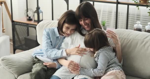 居心地の良いリビングルームで愛する家族 彼女の成長している赤ちゃんのバンプを優しく愛撫彼らの手はソファの上に一緒に座って 彼女の息子と娘を伴う妊婦 — ストック動画