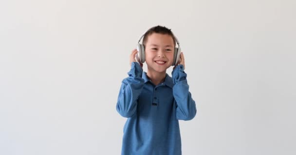 亚洲男孩沉浸在原始的白色背景下的音乐世界中 带着一副时髦的耳机装饰着他的耳朵 他迷上了旋律和旋律 — 图库视频影像