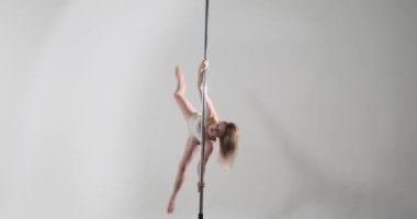 Kendine güvenen beyaz bir dansçının zarif direk dansı performansı. Gri bir arkaplanda, göz kamaştırıcı beyaz bir dans kıyafeti içinde, özgüven ve zarafet sergileyerek sahneye çıkıyor..