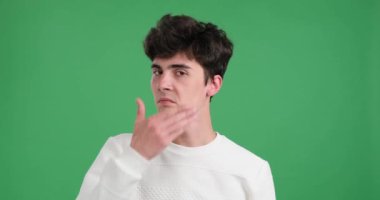 Ciddi bir beyaz adam yeşil arka planda yakalandı. Odaklanmış bir ifadeyle, elini ağzına kaldırarak sessizliği işaret ediyor. Onun yoğun bakışı ve hareketi mahremiyet arzusunu akla getiriyor..